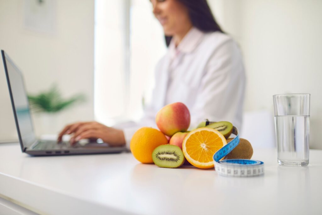 a dietitian vs nutritionist working at a laptop with fruit in the foreground