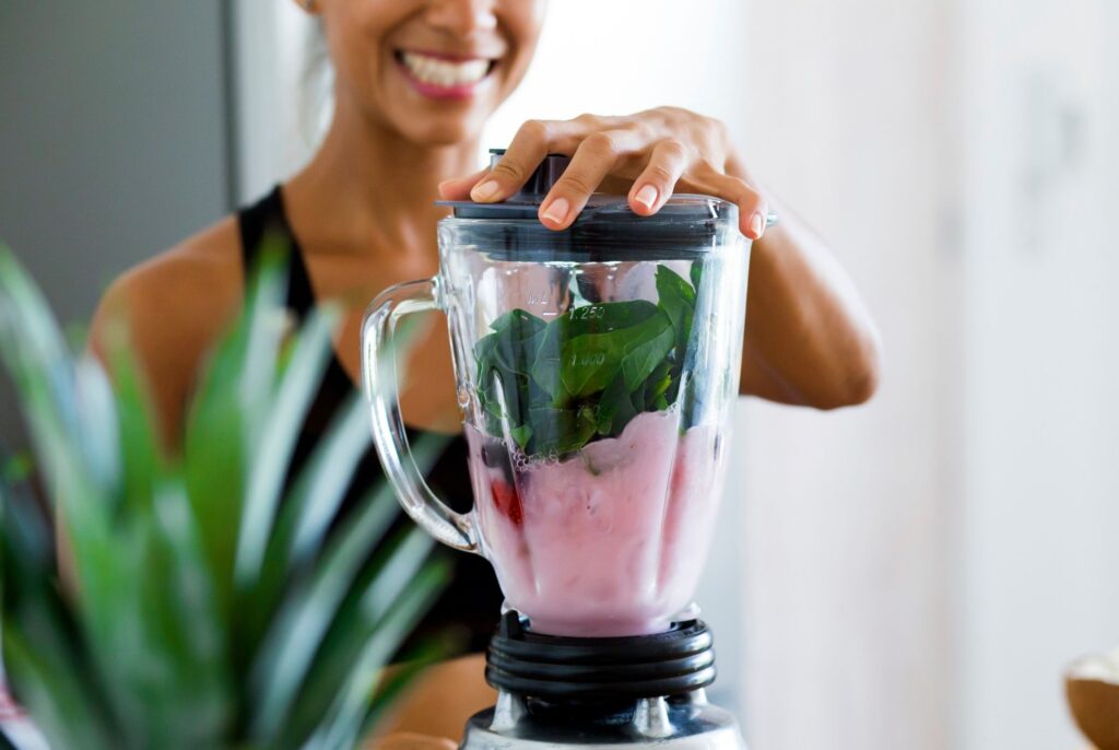 A women making a nutritious smoothie with greens and frozen fruit