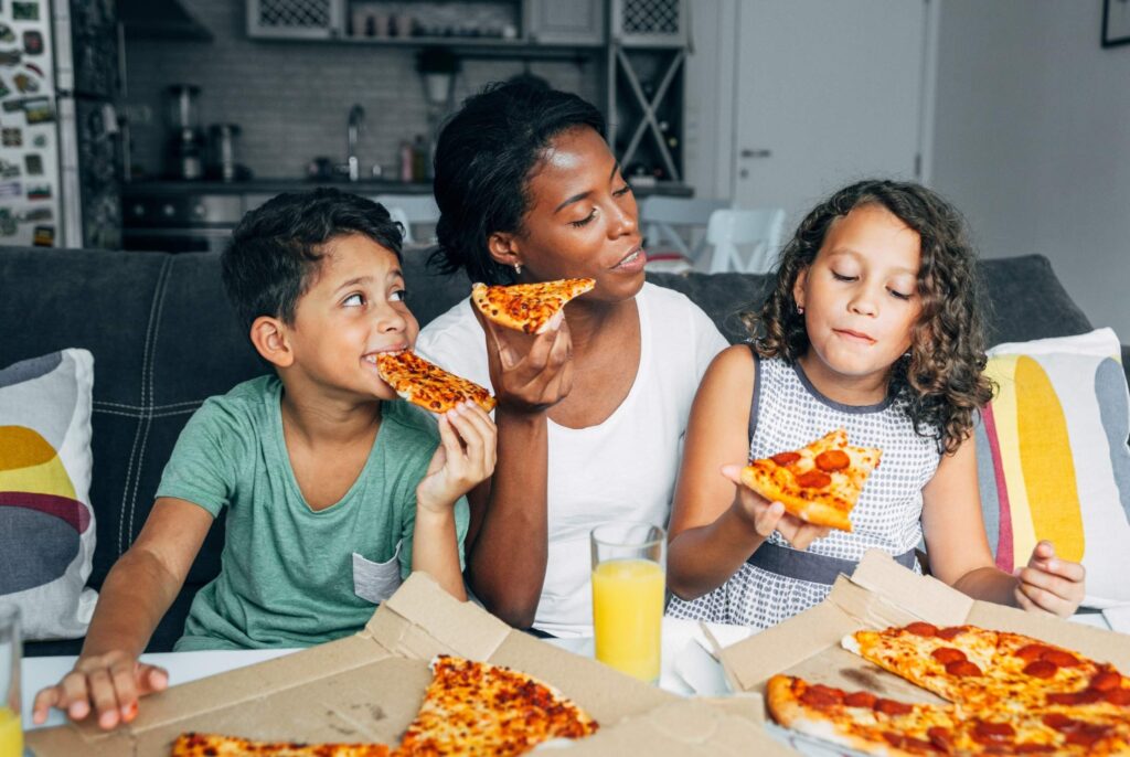 mom with kids eating pizza on the couch enjoying a meal together