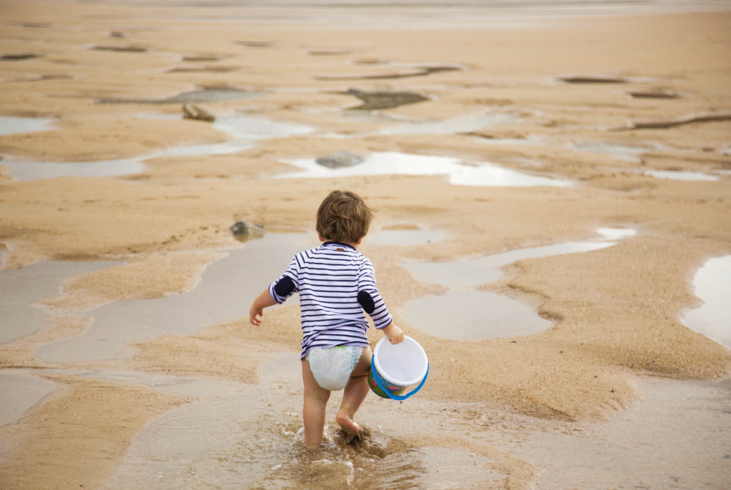 toddler holding a pail at the beach ready to explore