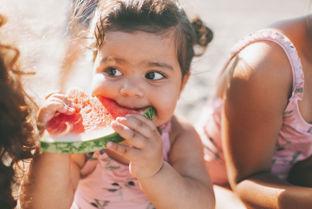 close up of a toddler eating beach snacks including watermelon