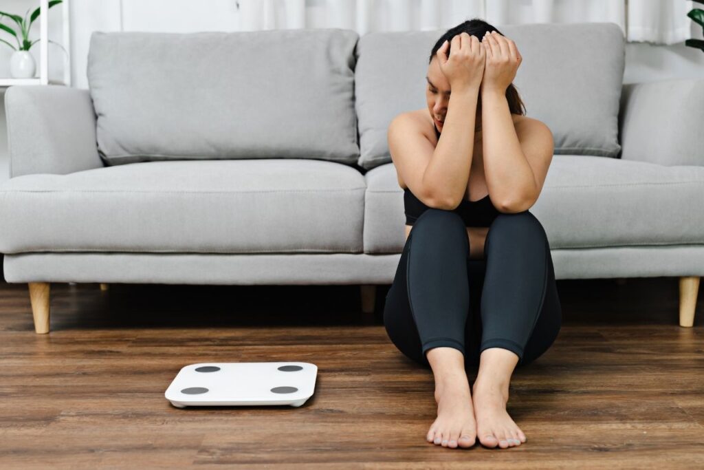 a woman is frustrated by struggles with weight loss and stares angrily at a scale on the floor