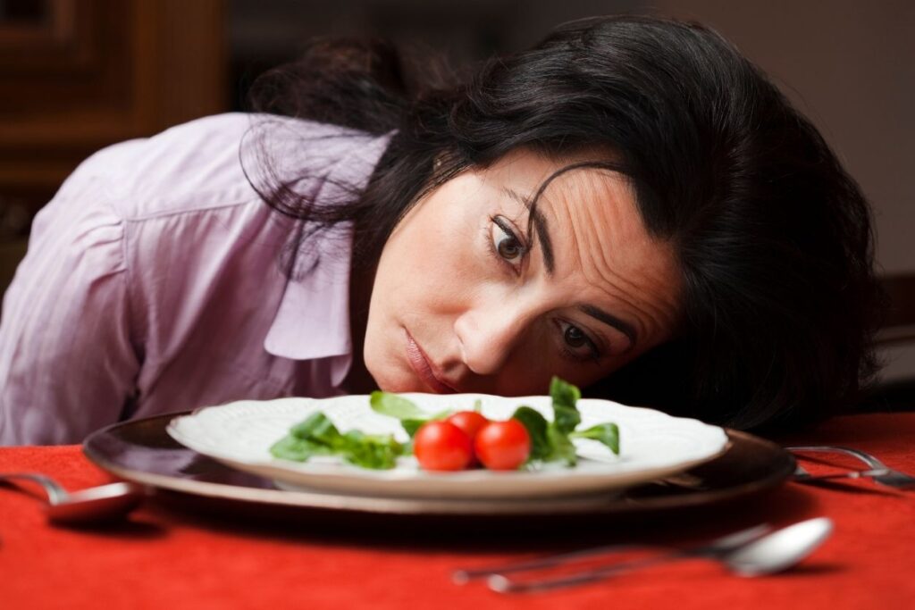 a woman affected by PCOS nutrition diet culture staring at a plate with a few veggies on it