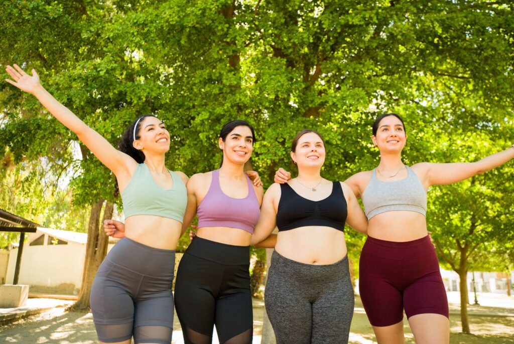beautiful happy group of diverse women with different bodies celebrating looking cheerful after running or exercising in the park, not afraid of diet culture