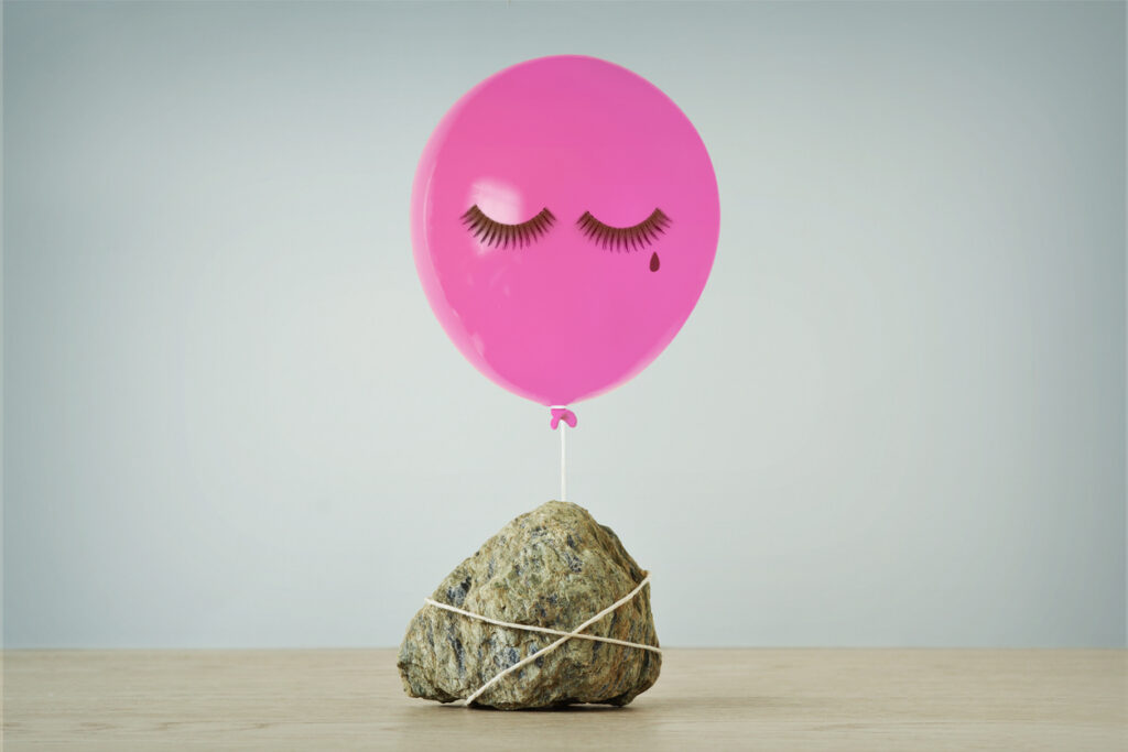 Pink balloon with sad expression tied to heavy stone - Concept of woman and freedom