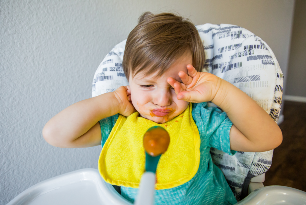 a small child being fed food on a spoon in hopes to prevent picky eating down the road