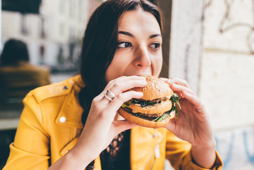 a woman eating a burger experiencing guilt and shame around eating the food
