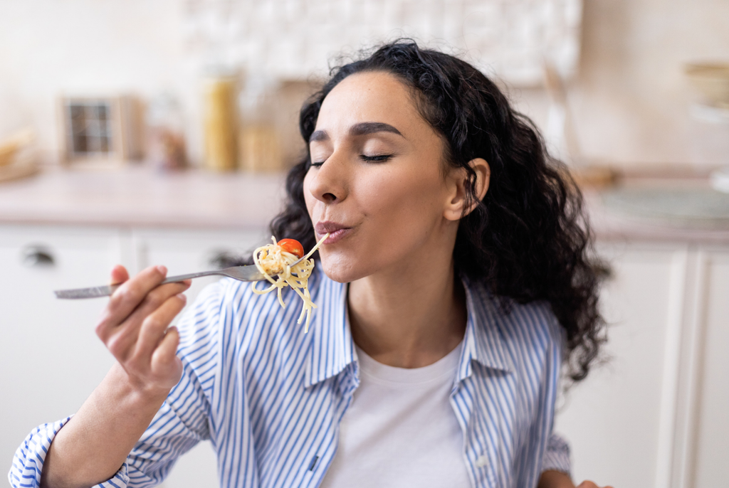 a woman eating spaghetti with her eyes closed, not experiencing food noise and just enjoying the food to herself