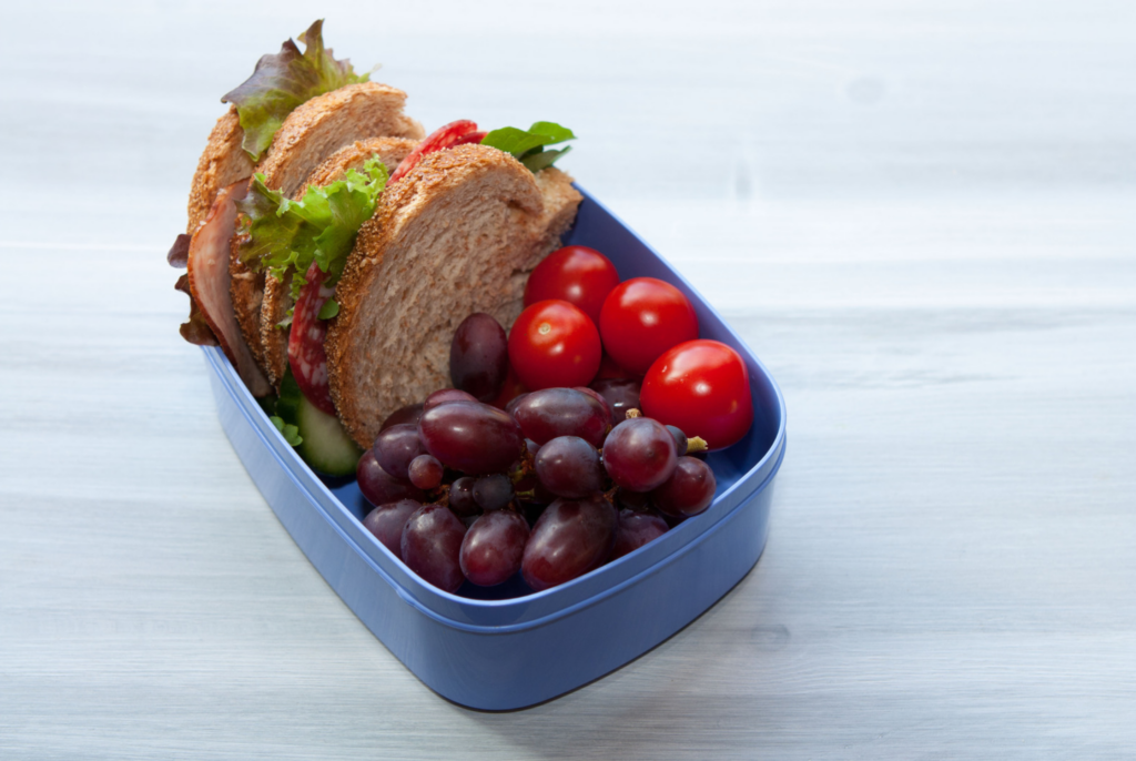 close up of a sandwich in a container with some fruit and tomatoes, perfect for after-school sports nutrition